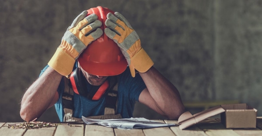 person wearing a reflective vest, hard hat, and work gloves holding their head