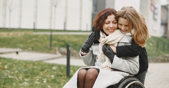 middle aged woman and teenage girl where winter attire and hugging, the older woman is in a wheelchair