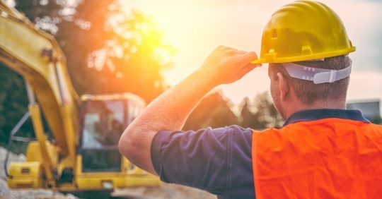 man wearing a hard hat and reflective vest looking at a backhoe machine