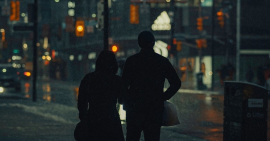 two people walking on a sidewalk at nighttime wearing oversized coats